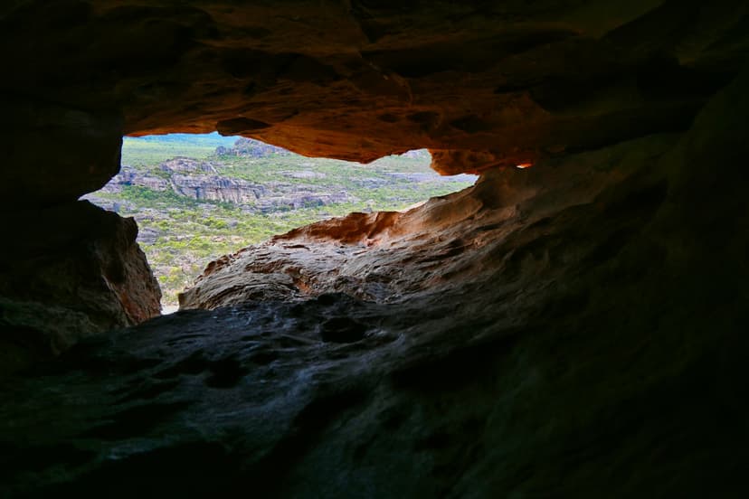 Rocky cave opening framing a view of forested landscape and rocky cliffs
